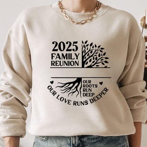 Pu&ograve; includere: Una felpa beige con la scritta "2025 Family Reunion" sopra una grafica ad albero. Sotto, la scritta "Our Love Runs Deeper" circonda una grafica di radici. La felpa ha maniche lunghe.