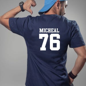 May include: Navy blue t-shirt featuring the name "MICHEAL" and the number "76" in white. The shirt is a solid colour and has a crew neck.