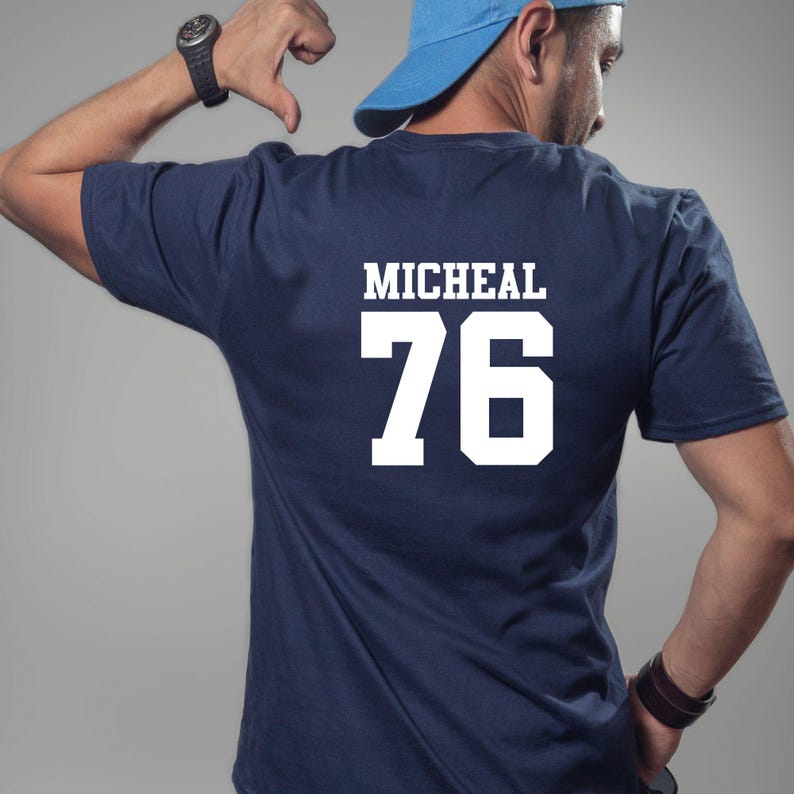 May include: Navy blue t-shirt featuring the name "MICHEAL" and the number "76" in white. The shirt is a solid colour and has a crew neck.