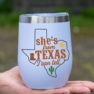 May include: White insulated wine tumbler with a silver rim. The tumbler features a Texas-shaped graphic with a cowboy boot, star, and cactus, along with the text "She's from Texas I can tell."