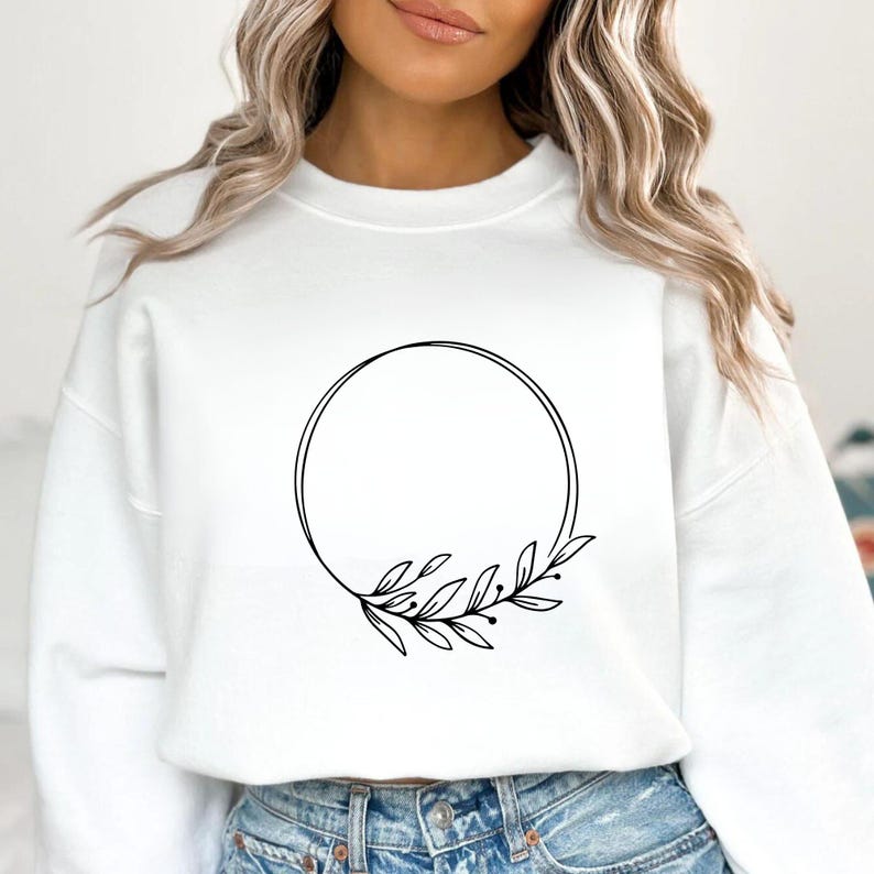 May include: White sweatshirt featuring a black circular design with a botanical leaf and berry accent. The design is centered on the front of the sweatshirt. The sweatshirt is made of a soft material.