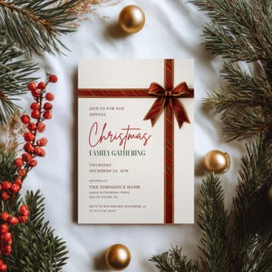 Könnte beinhalten: Eine cremefarbene Weihnachtseinladungskarte mit einem rot-grünen Schleifendesign. Die Karte lautet "Nehmen Sie an unserem jährlichen Weihnachts-Familientreffen teil" mit Datum, Uhrzeit und Ortsangaben. Goldene Ornamente und Tannenzweige umgeben die Karte.