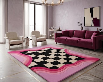 May include: A rectangular area rug featuring a central black and white checkered pattern surrounded by concentric, wavy borders in varying shades of pink and magenta, creating a layered, fluid design on a light-coloured floor surface.