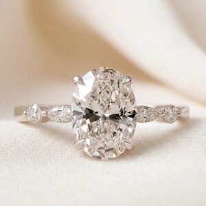 May include: A platinum engagement ring featuring an oval-cut diamond center stone. The ring has a delicate band with smaller round and pear-shaped diamonds. The large center diamond is held by four prongs.