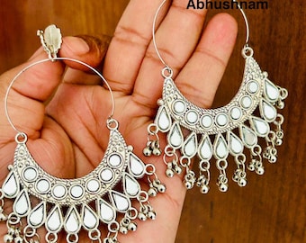 May include: Silver-toned hoop earrings with a crescent moon design. The earrings feature a series of round and teardrop-shaped mirrored accents, with small dangling beads at the bottom. The text "Abhushnam" is visible.