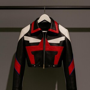 May include: Black leather jacket with a red star design on the front. The jacket features white accents on the shoulders and collar, with red and blue stripes on the sleeves. It has a zip-up front and a cropped fit.
