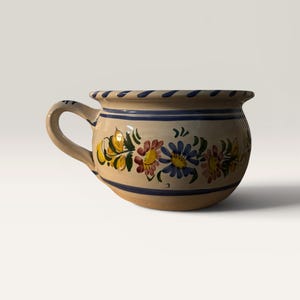 May include: A ceramic mug with a handle, featuring a beige base adorned with hand-painted floral designs in yellow, red, and blue. The rim and a band near the base are accented with blue stripes. The mug is designed with a rounded shape.