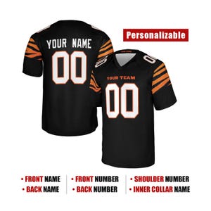 Könnte beinhalten: Ein schwarzes Trikot mit orangefarbenen Tigerstreifen an den Ärmeln, mit weißen Nummern 00 und dem Text YOUR NAME und YOUR TEAM. Das Design enthält den Text Personalizable, FRONT NAME, BACK NAME, FRONT NUMBER, BACK NUMBER, SHOULDER NUMBER und INNER COLLAR NAME.