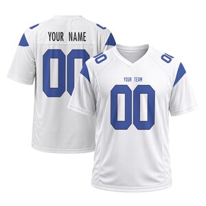 Puede incluir: Una camiseta deportiva blanca de manga corta con detalles azules en los hombros y números 00 azules en el frente y la espalda. El frente muestra el texto YOUR TEAM sobre el número, y la espalda muestra el texto YOUR NAME sobre el número.