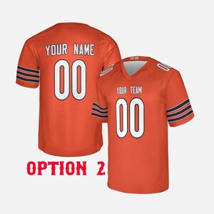 K&ouml;nnte beinhalten: Zwei orangefarbene Football-Trikots mit wei&szlig;en Zahlen und Schriftz&uuml;gen. Auf einem Trikot steht "YOUR NAME" und die Nummer "00" auf dem R&uuml;cken. Das andere Trikot zeigt "YOUR TEAM" und die Nummer "00" auf der Vorderseite. Beide haben marineblaue Streifen.