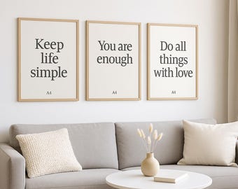 Puede incluir: Tres láminas enmarcadas con citas inspiradoras: "Keep life simple", "You are enough" y "Do all things with love". Las láminas se exhiben sobre un sofá gris con cojines decorativos y una pequeña mesa redonda.