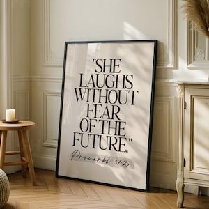 Könnte beinhalten: Ein rechteckiges gerahmtes Wandbild mit beigem Hintergrund und kräftiger schwarzer Serifenschrift mit dem Text "SHE LAUGHS WITHOUT FEAR OF THE FUTURE." Unter dem Haupttext steht "Proverbs 31:25" in einer kleineren schwarzen Schriftart.