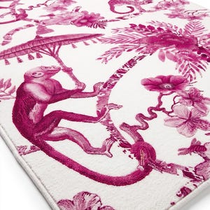 May include: A rectangular area rug featuring a white background with a repeating pattern of magenta monkeys, palm trees, and flowers. One monkey is depicted holding a parasol while perched on a tree branch, rendered in shades of deep pink.