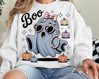 Könnte beinhalten: Ein weißes Sweatshirt mit einer Grafik eines hellblauen Geistes, der eine rosa herzförmige Sonnenbrille, eine rosa Schleife und eine Perlenkette trägt. Der Text Boo steht über dem Geist, umgeben von kleinen Kürbissen und Sternformen.