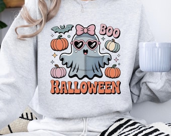 Könnte beinhalten: Ein hellgraues Sweatshirt mit Rundhalsausschnitt und einer Grafik eines Geistes mit herzförmiger Sonnenbrille und rosa Schleife. Das Design enthält Kürbisse, eine Fledermaus, Sterne sowie den Text "BOO" und "HALLOWEEN" in einer Retro-Schrift.