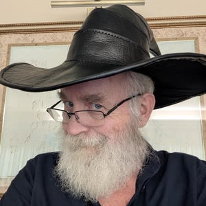 May include: A black leather hat with a wide, curved brim and a pointed, structured crown. The hat features visible stitched seams along the crown and the edge of the brim, creating a distinct layered appearance with a smooth, dark finish.