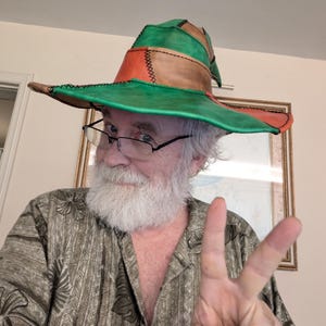May include: A patchwork hat with a wide brim, featuring green, orange, and brown leather panels stitched together. The hat has a pointed crown and a distinctive, handcrafted appearance. The hat is a unique accessory.