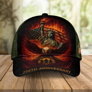 Könnte beinhalten: Eine schwarze Baseballkappe mit patriotischem Design. Die Kappe zeigt die Freiheitsstatue, eine amerikanische Flagge und einen Adler mit dem Text "250th Anniversary". Das Design ist vor einem feurigen Hintergrund platziert.