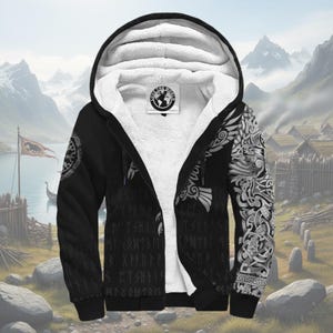 Könnte beinhalten: Schwarzer Kapuzenpullover mit Reißverschluss, weißem Sherpa-Futter und Kapuze. Die Jacke hat ein Wikinger-Motiv mit komplizierten Mustern auf den Ärmeln und dem Torso. Der Hintergrund zeigt eine malerische Landschaft.