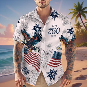 Puede incluir: Camisa blanca de manga corta con diseño patriótico. La camisa presenta una bandera estadounidense, un águila, fuegos artificiales y estrellas. El texto "1776 250 2026" está impreso en la parte delantera. Con cuello de campamento.