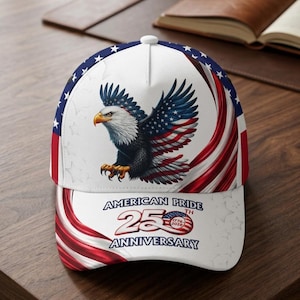 Könnte beinhalten: Eine Baseballkappe mit weißem Hintergrund, einem Weißkopfseeadler-Motiv, rot-blauen, flaggenartigen Wirbeln und Sternen. Der Text lautet AMERICAN PRIDE 250TH ANNIVERSARY mit einem kreisförmigen Emblem, das die Jahreszahlen 1776 und 2026 enthält.