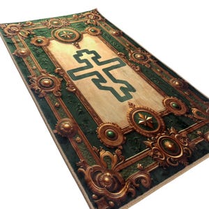 May include: A rectangular rug with an ornate design. The rug features a central beige panel with a green cross-like symbol. The border is dark green with gold-colored decorative elements, including medallions and floral patterns. The rug has a detailed, textured appearance.