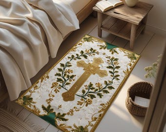 May include: A rectangular white rug with a gold cross design, surrounded by green and gold floral accents. The rug has a green border and is placed on a light-colored wooden floor. The rug is near a bed and a small wooden table.
