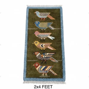 May include: A rectangular rug with a dark olive green background featuring six stylized birds in various colors including blue, pink, yellow, and brown. The rug has a light blue patterned border and white fringe on the top and bottom edges, measuring 2x4 feet.