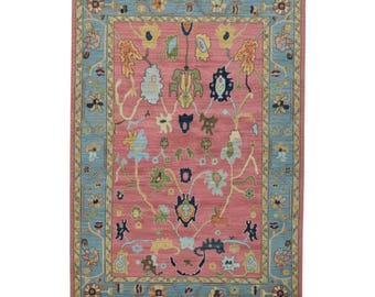 Könnte beinhalten: Rechteckiger Teppich mit einem rosa Mittelfeld und einem hellblauen Rand. Der Teppich hat ein Blumendesign mit gelben, blauen und grünen Akzenten. Der Rand hat ein sich wiederholendes Blumenmuster.