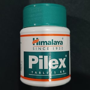 Könnte beinhalten: Eine weiße und türkisfarbene Flasche Himalaya Pilex Tablets 60. Die Flasche hat einen türkisfarbenen Deckel und ein weißes Etikett mit dem Himalaya-Logo und dem Text "SINCE 1930". Das Etikett zeigt auch das Wort "Pilex".