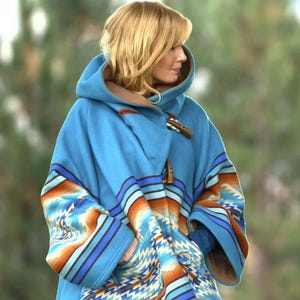 May include: A hooded blue poncho with a Southwestern-inspired pattern in shades of orange, blue, and white. The poncho features a toggle closure and is worn with blue jeans. The design includes a hood and pockets.