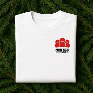 Könnte beinhalten: Weißes T-Shirt mit Rundhalsausschnitt und roter Grafik von sechs verbundenen Kreisen sowie dem Text "NUR NED HUDDLE" in Schwarz. Das Shirt besteht aus einem weichen Material und wird auf einem Hintergrund aus grünen Tannennadeln präsentiert.