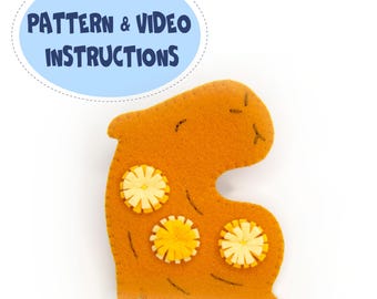 May include: A handmade orange felt capybara-shaped craft, decorated with three yellow flower embellishments. The image includes the text "PATTERN & VIDEO INSTRUCTIONS" in a blue oval. The background is white.