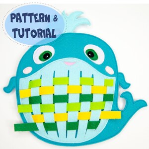May include: A felt whale toy in shades of blue, green, and yellow, with the text "PATTERN & TUTORIAL" in a blue oval. The whale features a woven design in its belly, with green and yellow strips. The whale has green eyes and a small pink mouth.