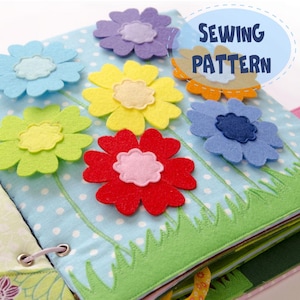 May include: A handmade felt book featuring colourful felt flowers in shades of blue, purple, yellow, green, red, and orange. The book has a light blue polka dot background with green grass and the text "SEWING PATTERN".