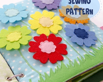May include: A handmade felt book with colorful felt flowers in shades of blue, purple, yellow, green, red, and orange. The book has a light blue polka dot background with green grass and the text "SEWING PATTERN".