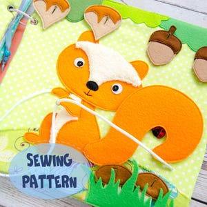 May include: A handmade felt sewing pattern featuring an orange squirrel with a white belly and tail, holding a white string. The background is light green with a polka dot pattern. The text "SEWING PATTERN" is visible. Acorns and grass are also included.