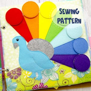 May include: A felt sewing pattern book featuring a blue bird and a rainbow design. The book has a floral pattern background and the words "SEWING PATTERN" in green. The rainbow includes red, orange, yellow, green, blue, and purple.