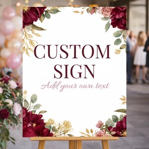 May include: A white custom sign with burgundy floral and gold leaf details. The sign reads "CUSTOM SIGN" with the text "Add your own text" below. The sign is displayed on a wooden easel, suitable for weddings or events.