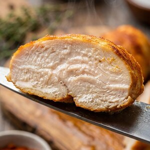 以下が含まれることがあります： 調理された鶏むね肉のクローズアップ。切り込みが入っており、ジューシーな白い肉が見える。外側は黄金色で味付けされた皮。切り口から湯気が立ち上り、出来立てであることがわかる。鶏肉はナイフで持たれている。
