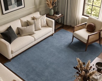 May include: A large, solid blue area rug with a soft, textured surface covering the floor in a living room. The rug is rectangular and features a uniform, deep blue color that spans the space between a cream sofa and a wooden armchair.