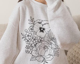 May include: A light gray heathered crewneck sweatshirt featuring a large black line art floral illustration on the front. The design includes detailed drawings of various flowers, leaves, and stems arranged in a central bouquet pattern.