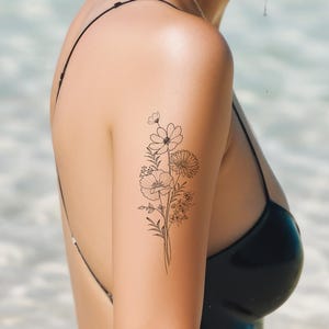 May include: A temporary tattoo of a delicate floral design featuring a bouquet of flowers with thin black lines. The tattoo is on a person's upper arm.