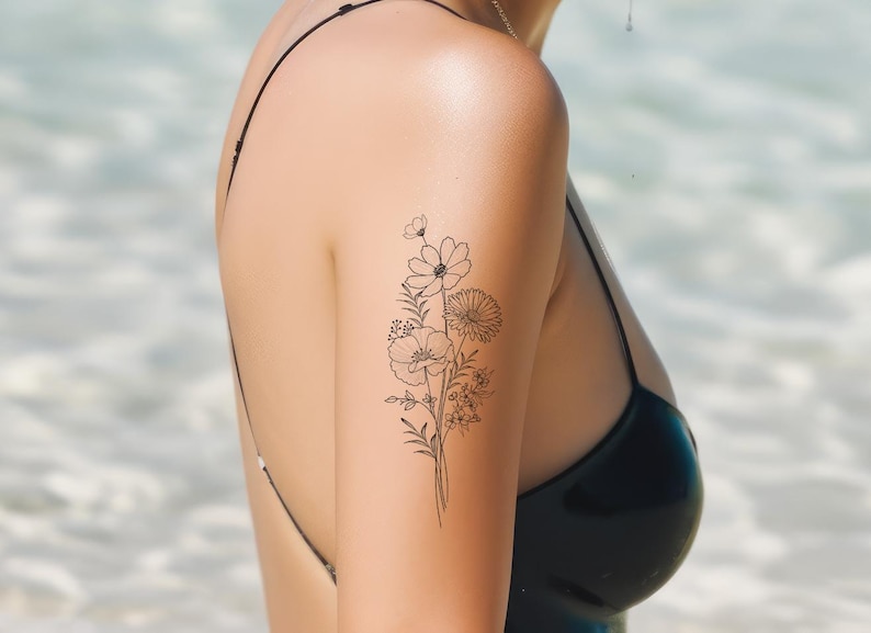 May include: A temporary tattoo of a delicate floral design featuring a bouquet of flowers with thin black lines. The tattoo is on a person's upper arm.