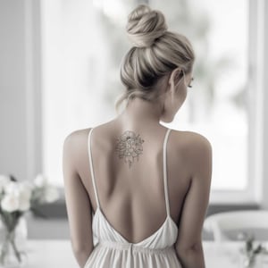 May include: A woman with blonde hair in a bun is wearing a white sleeveless dress with a floral tattoo on her back.