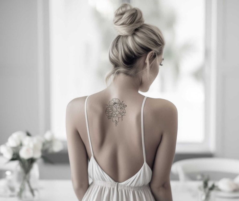 May include: A woman with blonde hair in a bun is wearing a white sleeveless dress with a floral tattoo on her back.