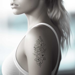 May include: A woman's shoulder with a black line drawing tattoo of a bouquet of flowers.