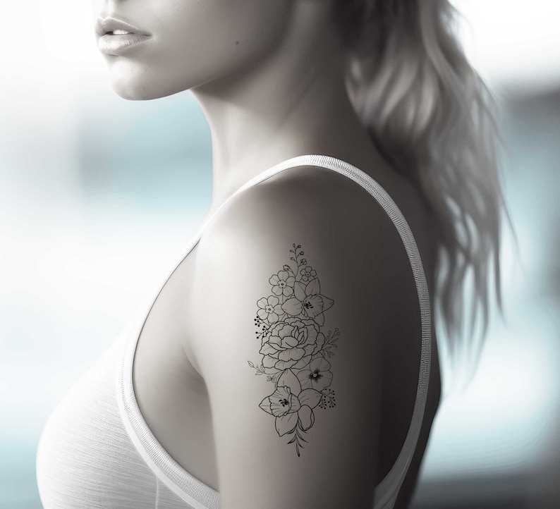 May include: A woman's shoulder with a black line drawing tattoo of a bouquet of flowers.