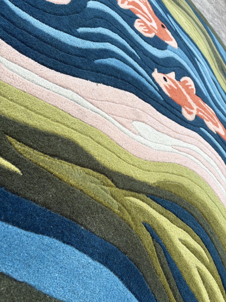 May include: A colorful rug with a water and koi fish design. The rug features shades of blue, green, pink, and orange. The design includes wavy lines to represent water and two orange koi fish swimming in the water.
