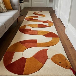 May include: A long, rectangular rug featuring a snake design. The snake's body is made of geometric shapes in orange, red, and yellow against a cream backdrop. The snake's head has a red tongue. The rug is placed in a hallway.